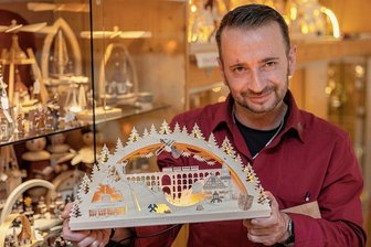 Neuer Vogtland-Schwibbogen aus Steinberg leuchtet auch ohne Netzanschluss - Der neue Vogtland-Schwibbogen mit LED-Lichtband aus der Drechslerei Kuhnert Rothenkirchen, den Verkäufer Robert Arnold präsentiert, leuchtet wahlweise mit Netzstrom oder Powerbank. 