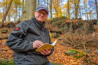 Neues Buch über den Poppenwald: „Die umfassendste Darstellung zur Schatzsuche im Westerzgebirge“ - Mario Ulbrich vor Reimanns Fels, einem der markanten Punkte im Poppenwald. Hier begann 1997 die Suche nach dem Bernsteinzimmer. Ein Vierteljahrhundert später sind noch immer Fragen offen.