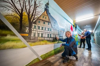 Neues Graffiti bringt erzgebirgische Tradition ins Schneeberger Kiez „Am Filzteich“ - Graffitikünstler Alexander Mehlhorn (l.) beim Gestalten der Fundgrube Wolfgangmaßen, mit Francis Möckel, der Bereichsleiterin Bildung und Programm, sowie dem Geschäftsführer des Kiez Frank Löffler.