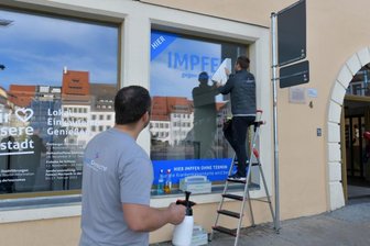 Neues Impfzentrum öffnet diese Woche - Sebastian und Robert Liebscher (von links) von der Firma Druckgemacht gestalteten am Montag das Schaufenster.