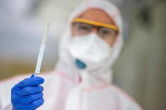 Ein Mitarbeiter hält in einem Abstrichzentrum einen Coronatest-Abstrich in der Hand.