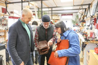 Nichts für Schnäppchenjäger: Handwerk statt Massenware in Lichtenau - Täschner Ulrich Czerny (Mitte) zeigt dem Ehepaar Kathrin und Marko Mallick wie eine alte Ledertasche aufbereitet wird. Zum 50. Geburtstag hatte die Unternehmerin von ihrem Mann die orange Tasche für 1600 Euro geschenkt bekommen.