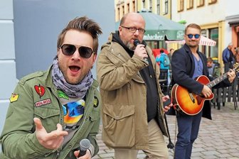 Ohne Geld durch Sachsen: Radiomoderator "Poschi" macht Halt in Freiberg - Tim Gernitz (l.) und Felix Günther (r.) von den Notendealern unterstützten Marcus Poschlod (Mitte) bei seinem Versuch, mit Gesang Geld zu verdienen.