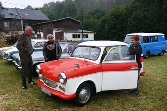 Oldtimertreffen im Erzgebirge: Regen trübt die Stimmung bei Neubelebung - Annett Stöhr und ihr Mann Rainer (Mitte) konnten ihren Trabi bei regnerischem Wetter zumindest einigen Gästen präsentieren.