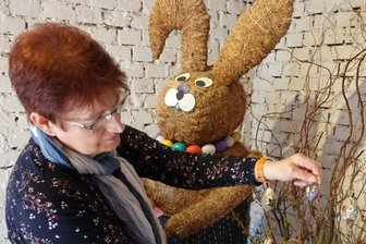 Parkschänke in Wildenfels stimmt auf Ostern ein - Annie Porstmann schmückt einen Strauß neben dem großen Osterhasen aus Stroh mit Ostereiern, die teils mit christlichen Motiven verziert worden sind.