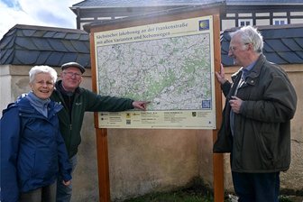 Pilgern durchs Erzgebirge: Vier Jakobswege führen von Sachsen bis nach Böhmen - Ulrich und Christina Kästli mit Pfarrer Sieghard Löser vor der Orientierungstafel Sächsische Jakobswege am Friedhof Elterlein.