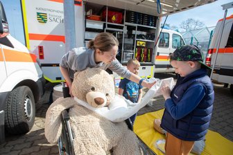 Plauener Autofrühling: Neue Blaulichtmeile begeistert junge Besucher - Auf der 6. Mobilitätsmesse in Plauen musste ein Teddybär versorgt werden. Unter Anleitung von Leonie Schneider von den Johannitern meisterten Leo (Mitte) und Magnus das Anlegen eines Verbandes.
