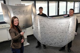 Porsche-Werkzeugbau Schwarzenberg öffnet sein Museum - Das Gästebuch im Museum des Porsche Werkzeugbaus in Schwarzenberg ist ungewöhnlich: Eine Motorhaube eines Sportwagens ist schon voller Signaturen. Das zeigen Jonas Voike und Nick Richter (r.). Anne Weber (vorn) von der Geschäftsleitung leitet das Projektteam „Museum“.