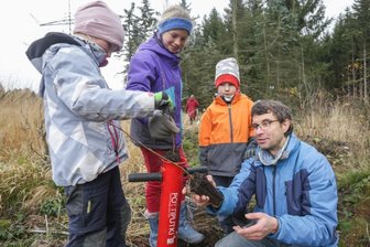 Projekt: Für jeden Einwohner ein neu gepflanzter Baum - Martin Gerner vom Projekt "Mein Baum, mein Chemnitz" pflanzt mit Selma, Joana und Rufus (von links) eine Erle an. Sie wird mithilfe eines Pflanzrohrs im Boden verankert. Auf einem Gebiet nahe der A4, auf dem früher Fichten angepflanzt wurden, soll so ein neuer Erlenbruchwald entstehen. 
