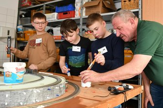 Rammstein spielen auf der Platte und gesteuert wird per Tablet: Modellbahnverein in Rochlitz begeistert Schüler - Im GTA-Angebot bauen Dominik, Oskar und Elias (v. l.) mit Vereinschef Uwe Uhlig an „ihrer“ Anlage.