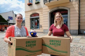 Reichenbach: Stadtwerke ziehen wegen Hallenbad-Sanierung um - Nadine Pursch (l.) und Johanna Freund von der Kundeninformation der Stadtwerke mit Umzugskartons vor der Sparkasse am Postplatz. Dort werden sie ab Montag arbeiten.