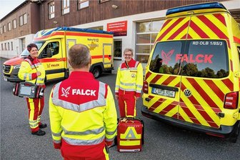 Rettungsdienst im Erzgebirge: Erneut rumort es hinter den Kulissen - Die Notfallsanitäter Katja Mehner, Roy Buschmann und Katharina Beyrich (v. l.) haben sich in ihrer markanten Falck-Einsatzkleidung für ein Foto vor die Rettungswache in Olbernhau gestellt. Links im Bild ist ein Rettungswagen (RTW) und rechts ein Krankentransportwagen (KTW). Falck betreibt diese Rettungswache bereits seit 2019.