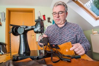 Rico Wappler hat was gegen kalte Finger - Handschuhmacher Rico Wappler an seiner Nähmaschine. Vor sich hat er einen der Spezialhandschuhe. Der Akku steckt hinter einem Reißverschluss an der Seite, das schwarze Band ist das Heizelement. 