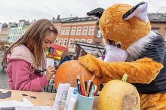 Rodewischer Herbst- und Kreativmarkt erlebt Bilderbuchpremiere - Der 1. Rodewischer Herbst- und Kreativmarkt auf dem Postplatz war am Samstag sehr gut besucht. Viele ehrenamtlich Mitwirkende wie die Freiwillige Feuerwehr, Genuss im Fachwerk, die Landeskirchliche Gemeinschaft und andere mehr trugen mit liebevoll gestalteten Ständen dazu bei. Bei "Rock A Fox" konnte man Kürbisse bemalen, wovon die siebenjährige Anna gern Gebrauch machte.