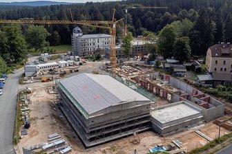 Sachsens neue Forstschule in Bad Reiboldsgrün: Die Kosten steigen - Kräne drehen sich, Rohbauten wachsen in die Höhe: Bad Reiboldsgrün ist eine Großbaustelle. Hinten im Bild: der historische Komplex mit Kurhaus (erkennbar am Turm), Casino und einem weiteren (hier nicht sichtbaren) Gebäude. Dort entstehen Wohnheim, Verwaltungstrakt, Versorgungszentrum und ein Gästehaus zu Fortbildungszwecken. Im Vordergrund: ein Neubau-Karree mit Maschinenhalle und Werkstattgebäuden, die sich um einen Wirtschaftshof gruppieren. Der Berufsschulbetrieb soll im September 2022 starten. 