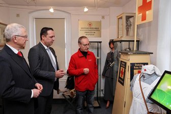Sächsisches Rot-Kreuz-Museum Beierfeld: Selbst Sachsens DRK-Präsident zeigt sich beeindruckt - Sachsens DRK-Präsident Peter S. Kaul und Landrat Rico Anton wurden von André Uebe (v. l.), dem Vorsitzenden des DRK-Ortsvereins, durch das Sächsische Rot-Kreuz-Museum in Beierfeld geführt.