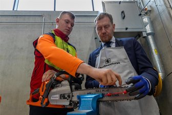 Sägeketten schärfen und vieles mehr – Ministerpräsident weiht Forstzentrum in Bad Reiboldsgrün ein - Azubi Phil Mühlmann (links) zeigt dem sächsischen Ministerpräsidenten Michael Kretschmer, wie das mit dem Sägekettenschärfen funktioniert.