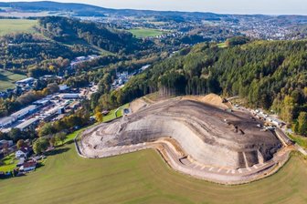 Sanierung der Halde "Knochen": Halbzeit auf der Großbaustelle - Diese Drohnenaufnahme aus der Luft zeigt den aktuellen Stand der Haldensanierung und die erkennbare, neue Profilierung des "Knochens" in Raschau-Markersbach. Seitlich an der Halde ist bereits das neue Regenrückhaltebecken zu sehen, ebenso wie die begonnene Umfahrung.