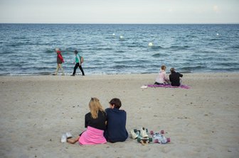 Schleswig-Holstein: App-Anmeldung für Strandbesuch an der Ostsee geplant - Schleswig-Holstein, Scharbeutz: Paare sitzen und gehen in einigem Abstand zueinander am Strand der Gemeinde Scharbeutz im Kreis Ostholstein.