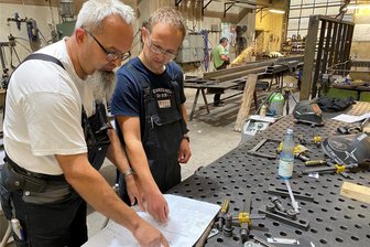 Schlosserei Zirnstein Reichenbach: Warum der Meister bis 76 durchziehen muss - auch wenn die Arbeit auf die Knochen geht - Hinten fliegen die Funken, vorn wird eine technische Zeichnung studiert. Arbeitsalltag in der Reichenbacher Schlosserei Zirnstein. Metallbauermeister Patrick Zirnstein im Gespräch mit Geselle Steve Hammerl.