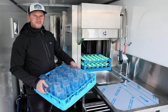 Schöner feiern: Partymacher aus Schwarzenberg setzt auf Spülautomat und Luxusklo - Patrick Weigel am mobilen Spülautomat. Rechts werden die Körbe mit Mehrweggeschirr hineingestellt. Sie laufen von selbst durch und werden links sauber ausgespuckt. Der Automat ist in einem Anhänger installiert.