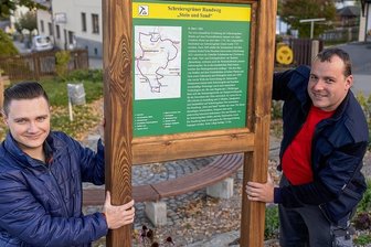 Schreiersgrün: Wandern auf den Spuren von "Stein und Sand" - Lucas Linder (links) und Nils Fischbach vom Förderverein Feuerwehr Schreiersgrün montieren die Infotafel zum Rundwanderweg auf dem Dorfplatz am Feuerwehrdepot. Dort beginnt die 7 Kilometer lange Tour "Stein und Sand".