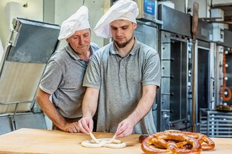 Schreiersgrüner Bäcker lässt nichts anbrennen: Riesen-Brezel von der Sternquell-Wiesn kommt ins Sortiment - Der eine Bäckermeister schaut dem anderen über die Schulter: Kai Goldmann, seit vorigem Jahr im Team der Feinbäckerei Wunderlich in Schreiersgrün, zeigt seinem Chef Volker Wunderlich, wie die perfekte Wiesn-Brezel gelingt.