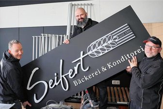 Schwarzenberg: Ladenumbau vor Ostern im Eiltempo -  "Das war schon sportlich", so der Chef Patrick Seifert, der am Dienstag gemeinsam mit den beiden Tischlern der Firma Trommler, Jörg Reiband (l.) und Hendric Lindner (r.), nicht nur das neue Werbebanner stemmte. 