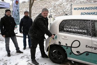 Schwarzenberger Stadtteil Sonnenleithe hat seine erste öffentliche Ladesäule für E-Autos - Stadtwerke-Geschäftsführer Sascha Wehrmann "zapft" Strom an der neuen Station. Zur Eröffnung im Flockenwirbel dabei: Enrico Schaarschmidt (l.) und Michael Förster von der Wohnungsgenossenschaft.