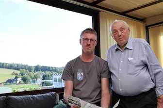 „Schwarzer Montag“: Wie ein Erzgebirger die Luftschlacht 1944 erlebte - Zeitzeuge Werner Pech (rechts) gibt Frank Retzlaff noch einige Zeitungsartikel über die Luftschlacht. Im Hintergrund sieht man die damalige Absturzstelle.