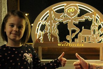 Schwibbögen aus Lengenfeld mit Heimatmotiv: "Jeden Tag ein Augenschmaus" - Daumen hoch für den Waldkirchen-Bogen mit dem verschmitzt rüberkommenden Waldkirchen-Maskottchen Edwin. Tina Hartisch und Tochterherz Yara vor dem Heinzmann-Bogen, der das Fenster im Hausflur schmückt.