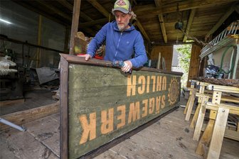 Sein Haus und seine Kulissen sind im Erzgebirgskrimi: So wichtig ist dieser Bernsdorfer für die Dreharbeiten - Benjamin Hahn nimmt in seiner Werkstatt das Schild fürs fiktive „Sägewerk Uhlich“ auseinander, das während des jüngsten Drehs am Lichtensteiner Sägewerk von Reiner Süß angebracht war. Hahn hatte diese Location empfohlen.