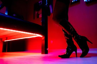 Sexarbeit trotz Verbots: So ist die Lage im Rotlichtmilieu in Mittelsachsen - Eine Prostituierte steht an einem rot beleuchteten Bett in einem Studio (Symbolfoto). Sexarbeit ist auch im Landkreis Mittelsachsen Alltag.