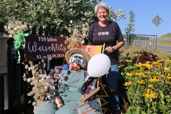 So humorvoll hat sich Weischlitz fürs große Dorfjubiläum herausgeputzt - Angelika Schantora zeigt die von ihr und Ehemann Karli gestaltete Figur nebst Bier, Luftballons und Begleitgrün. Das Enkelkind half auch mit.