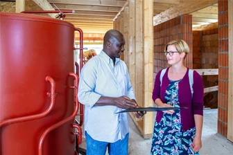 Solarhaus in Braunsdorf: Wie hohe Bauzinsen die Energiewende ausbremsen - Susanne Krautz ist eine der künftigen Bewohnerinnen des Solarhauses in Braunsdorf. Zum Richtfest kam sie mit Bauleiter Mohamed Sow von der Fasa ins Gespräch. Der wassergefüllte Solarspeicher wird noch von einer Trockenbauwand umkleidet.