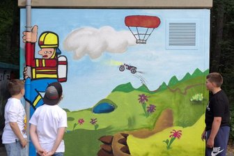 Spraydosen statt Sonnencreme: Kunstprojekt in Brand-Erbisdorf bringt noch mehr Farbe ins Erzengler Naturbad - Luca Watzl (r.), 13, erklärt das Motiv des Dino-Krokodils und der fliegenden Simson.
