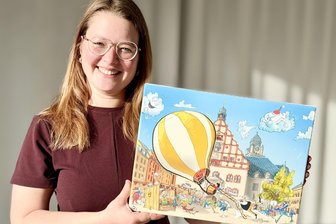 Tägliche Gewinnchance: Plauen startet zum zehnten Mal einen Online-Adventskalender - Lena Schaller vom Dachverband Stadtmarketing präsentiert einen der Tagespreise – ein Wimmelbild gedruckt auf Leinwand.