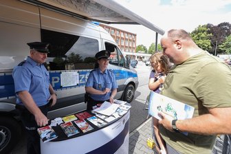 Tatort Burgstädt: Warum die Polizei am Rewe-Parkplatz steht - Roy Gotthardt mit seiner dreijährigen Tochter Charlize am Polizei-Präventionsmobil auf dem Rewe-Parkplatz in Burgstädt. Polizeiobermeister Robin Kinder und Polizeihauptmeisterin Kathy Seyferth informieren über Einbruchsschutz.