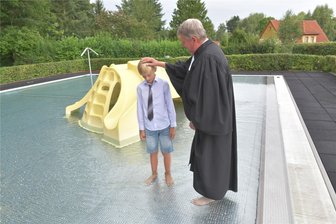 Taufe im Freibad: Wie die Schildkröte Rosalie ins Planschbecken von Reinsberg kam - Im Badepark Reinsberg taufte Pfarrer Karsten Loderstädt den zehnjährigen Wendel im Kinderbecken. Im Hintergrund die Spielschildkröte Rosalie, die Thema im Gottesdienst war.