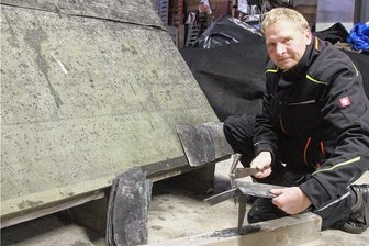 Thumstädters steigen den Leuten in Elsterberg und Umgebung seit 70 Jahren aufs Dach - Dachdeckermeister Sven Thumstädter zeigt das Dacheindecken mit Schiefer auf einem Dachmodell. Dazu bearbeitet er auf einer Haubrücke einen Schiefer mit dem Schieferhammer (im Vordergrund), um diesen in die notwendige Form zu bringen.