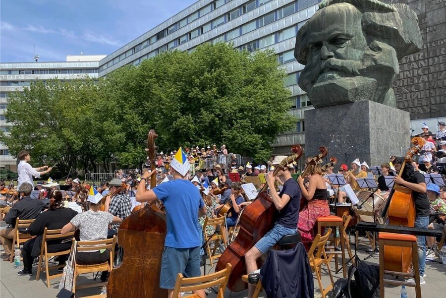 Trotz Sommerhitze: Musiker proben am Marx-Monument in Chemnitz - Fast 200 Musiker aus verschiedenen Ländern haben sich für gemeinsame Proben am Karl-Marx-Monument in Chemnitz zusammengefunden. Wegen der Hitze haben sich viele von ihnen mit Sonnenhüten aus Papier ausgestattet.