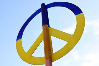 Bei einer Mahnwache zum Ukraine Krieg wird ein Friedenssymbol in den Farben der Ukraine in den Himmel gehalten.