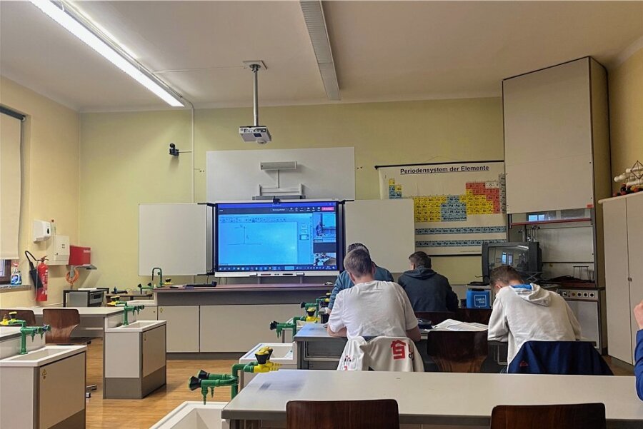 Unterricht 2.0 in Sachsen: Wenn ein Kurs von einem Lehrer an zwei Schulen gleichzeitig unterrichtet wird - Vier Elftklässler aus Niesky im Physik-Leistungskurs mit blauem Mikro-Würfel. Lehrer und "Tafelbild" sehen sie vorn auf dem Bildschirm. 
