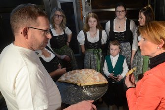 Unterwegs in Sachsen: MDR setzt „Erdäpfelkuhng“ aus dem Vogtland ein filmisches Denkmal - Über Kartoffelkuchen aus dem Vogtland plaudert Bäcker Jan Hartmann mit TV-Moderatorin Beate Werner im Beisein der Grünbacher Folkloristen.