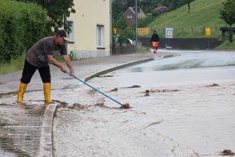 Unwetter über Frankenberg: Braune Brühe schießt über Straßen - Ein Anwohner von Sachsenburg versucht mit einem Besen den Gully frei zu halten.