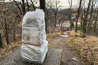 Vandalismus in Wildenfels: Denkmal im Schlosspark beschädigt - Nach der Beschädigung ist das Denkmal inzwischen mit Folie gesichert, damit keine Feuchtigkeit in den Sockel aus rotem Wildenfelser Marmor eindringt. Im Hintergrund der sogenannte Schwesternsitz, ein Aussichtspunkt auf einem Felsvorsprung.