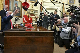 Vereinigte Staaten: Das Weiße Haus entscheidet, wer über Trump berichten darf - US-Präsident Donald Trump (links vorn) wirft im Beisein von Handelsminister Howard Lutnick (dahinter) und Pressesprecherin Karoline Leavitt (rotes Kostüm) eine Kappe in die Reihen der Medienvertreter im Oval Office.