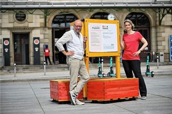Visionen für lebenswerte Plätze: Ein Aktionstag auf dem Bahnhofsvorplatz - Moderator Stefan Tschök und Landschaftsarchitektin Andrea Alter testen die neuen Sitzgelegenheiten vor dem Bahnhof. 