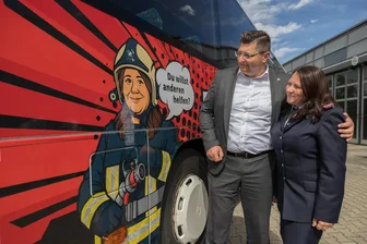 Vogtland: Zwei Schulbusse werben mit Comics für Teamgeist und Hilfsbereitschaft - Feuerwehrfrau Sandra Neubert und Landrat Thomas Hennig an einem der Busse.