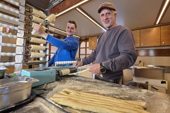 Von Baumstriezel bis Hotdog: Welche Leckereien beim Ostervolksfest in Plauen locken - Sascha Schmidt (rechts) und sein Sohn Dominic Schmack (links) aus Oberviechtach stellen auf dem Ostervolksfest in Plauen frische, handgemachte Baumstriezel her.